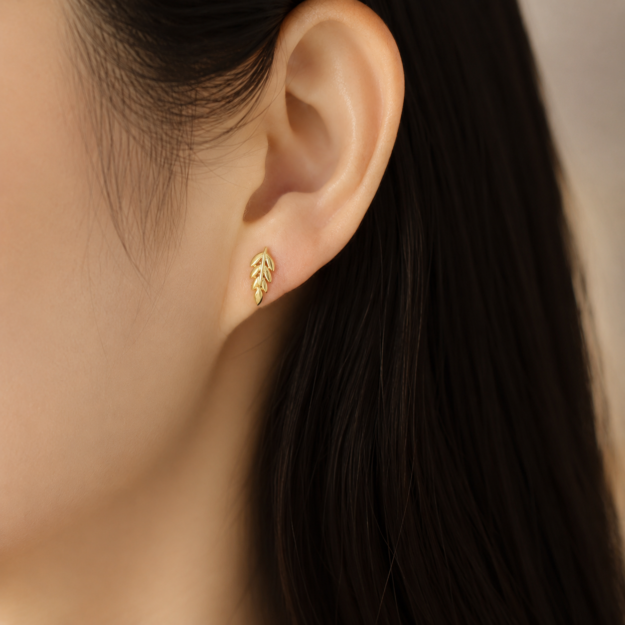 A close-up of a model's ear wearing a small gold leaf stud earring.