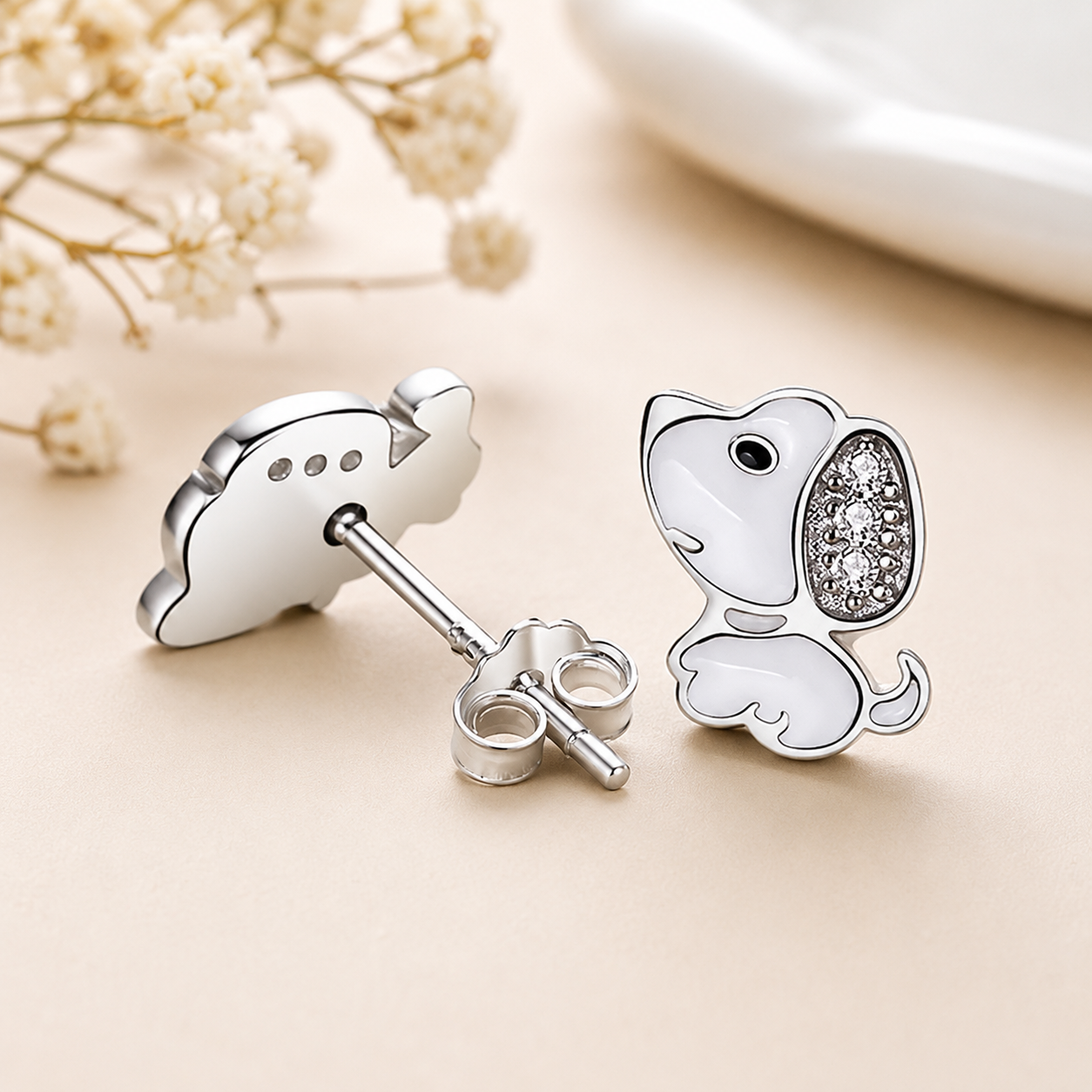 Silver dog-shaped earrings with clear gemstones on a beige surface.