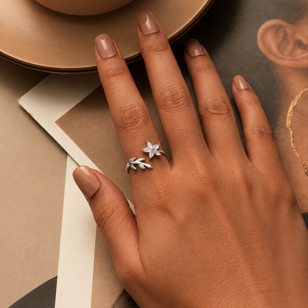 Hand wearing a silver ring with a floral design on a neutral background