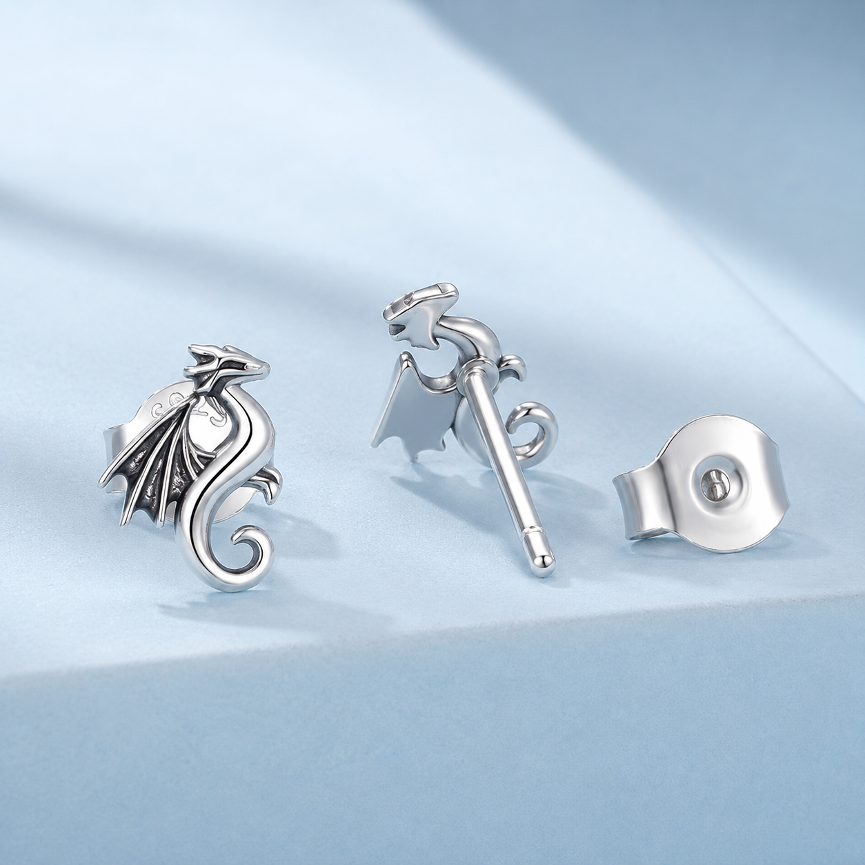 Silver earrings with dragon design on a light blue background