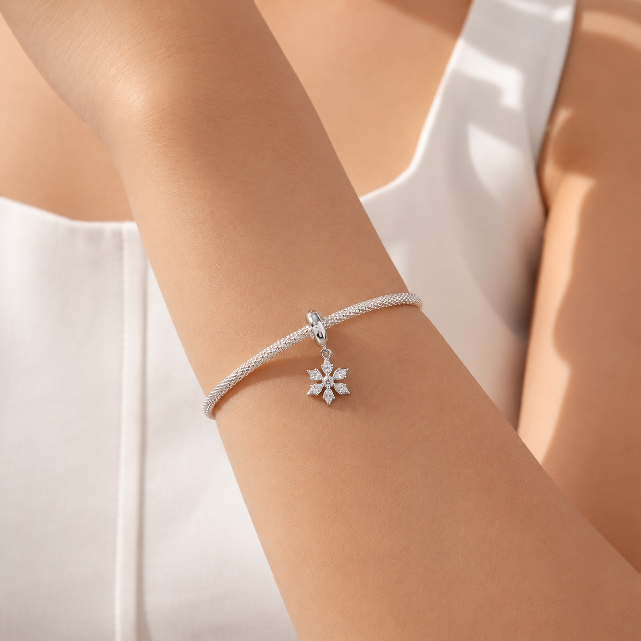 Silver bracelet with a snowflake charm on a person's wrist against a white background
