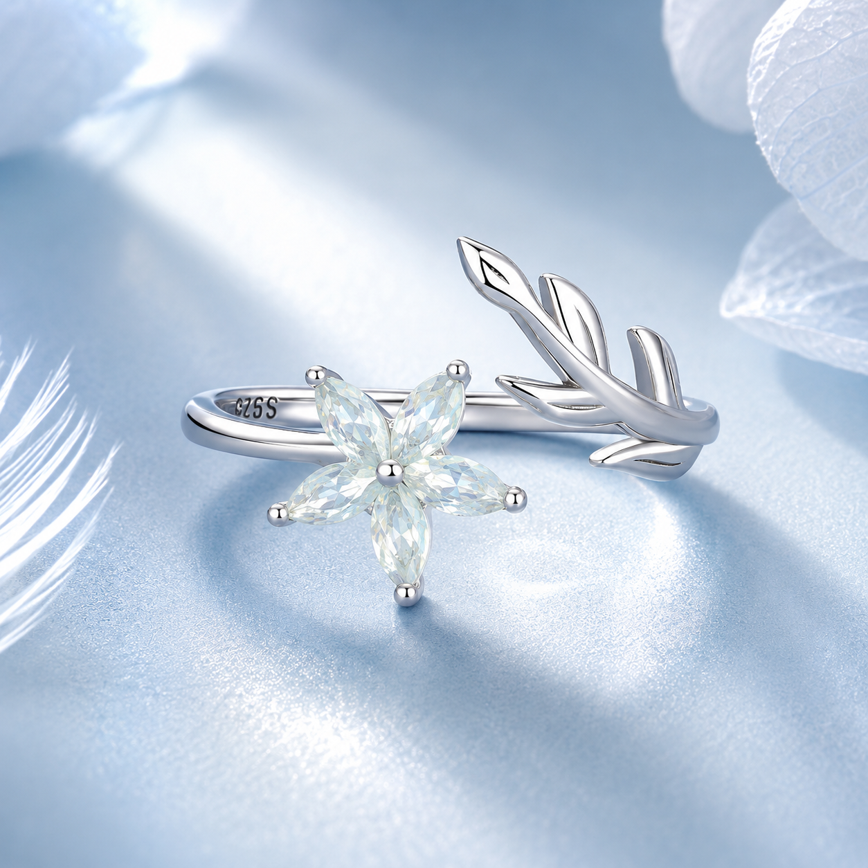 Silver ring with leaf design and gemstone on a light blue background