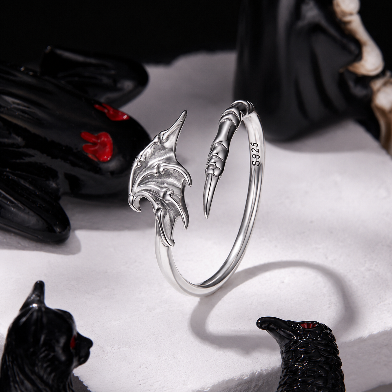 Silver dragon-shaped bracelet on a white surface with black gloves and figurines.