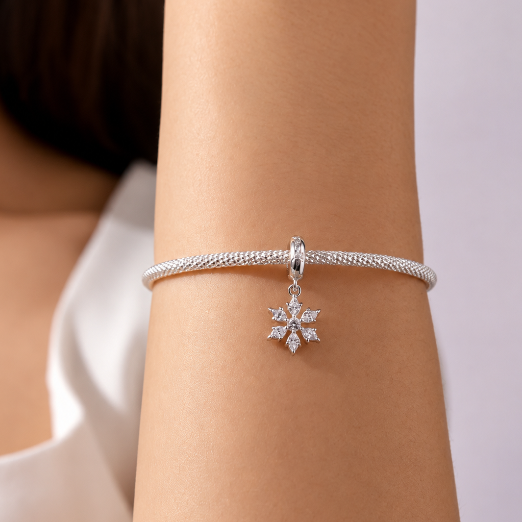 Silver bracelet with a snowflake charm on a wrist against a neutral background