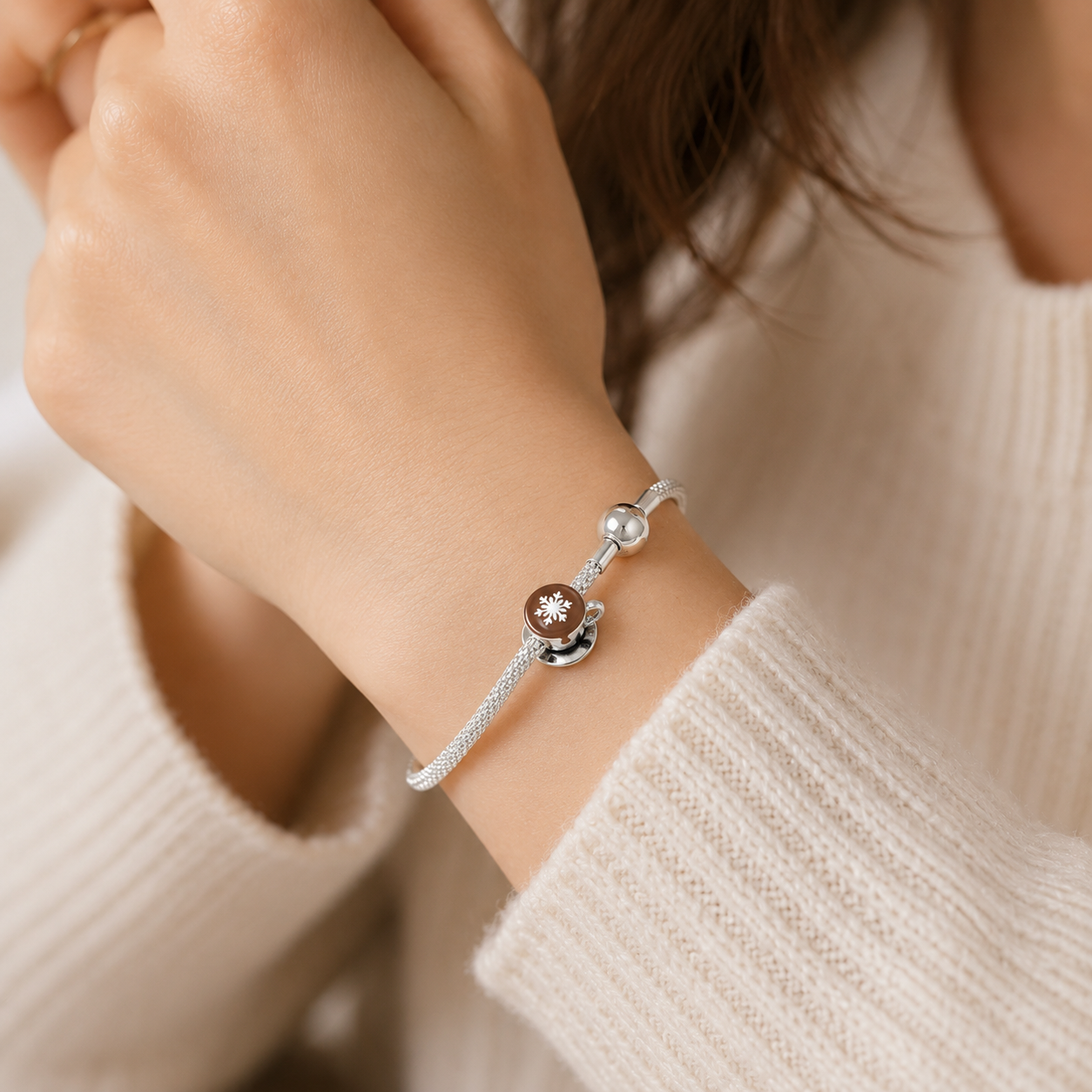 Close-up of a wrist wearing a silver bracelet with two charms against a neutral background