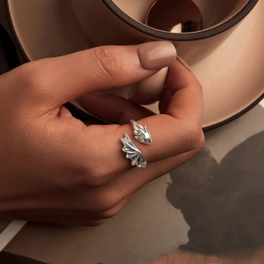 Hand wearing a silver ring with a delicate design, holding a ceramic mug.