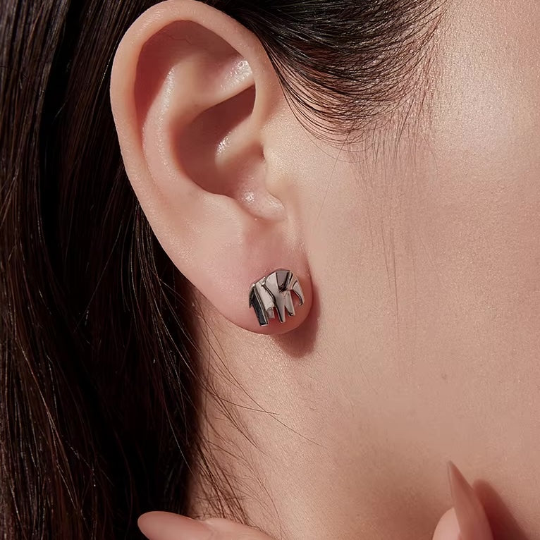 Close-up of an ear wearing a silver earring with 'MK' initials.