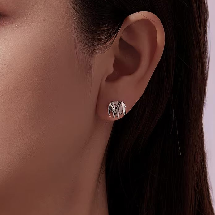 Close-up of an ear wearing a silver earring with a geometric design.