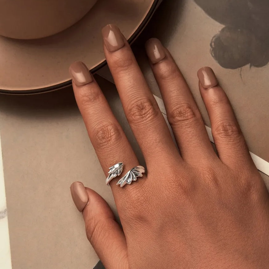 Hand wearing a silver ring with a detailed design on a neutral background