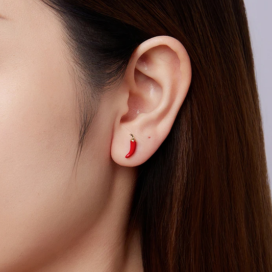 Close-up of an ear with a red chili pepper earring on a neutral background
