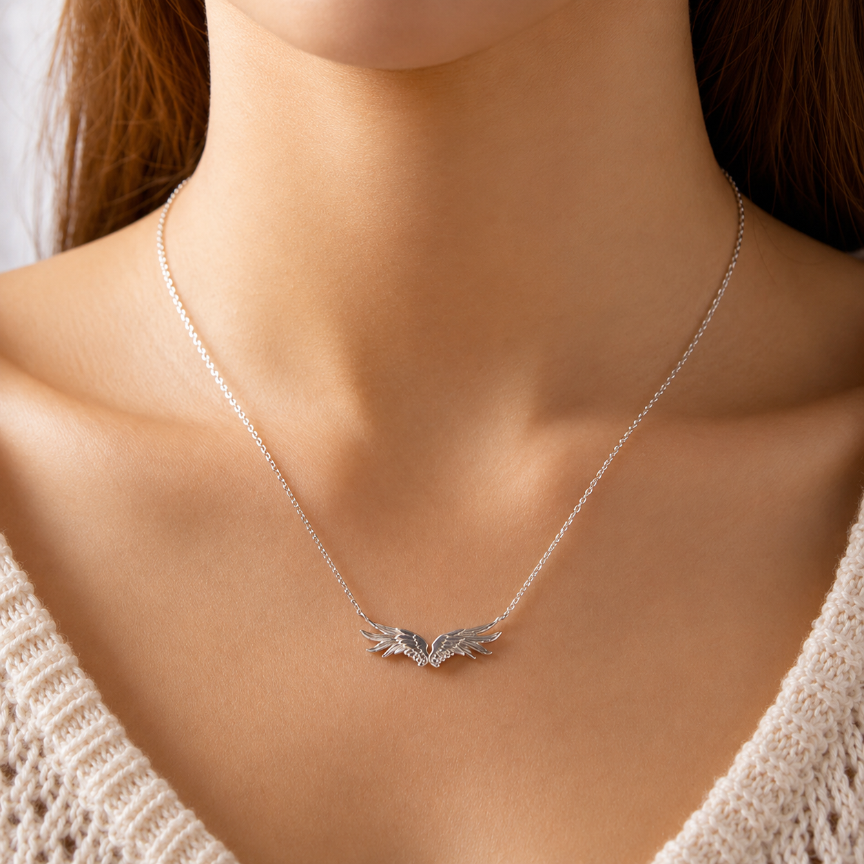 Silver necklace with angel wings pendant on a model wearing a beige sweater.