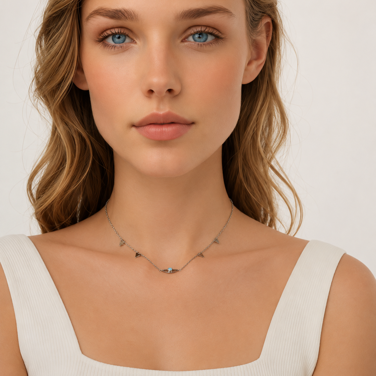 A close-up of a woman wearing a delicate silver necklace with small geometric charms, including a central blue stone, against a clean white background.