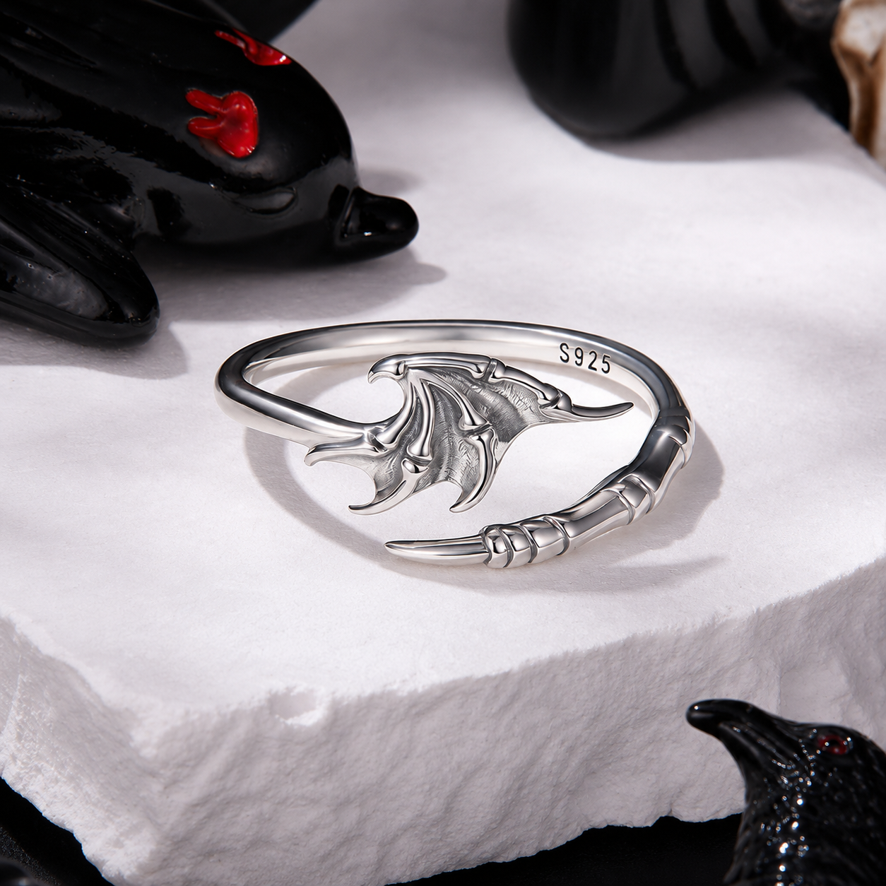 Silver dragon-shaped ring on a white surface with black gloves and red heart accents.