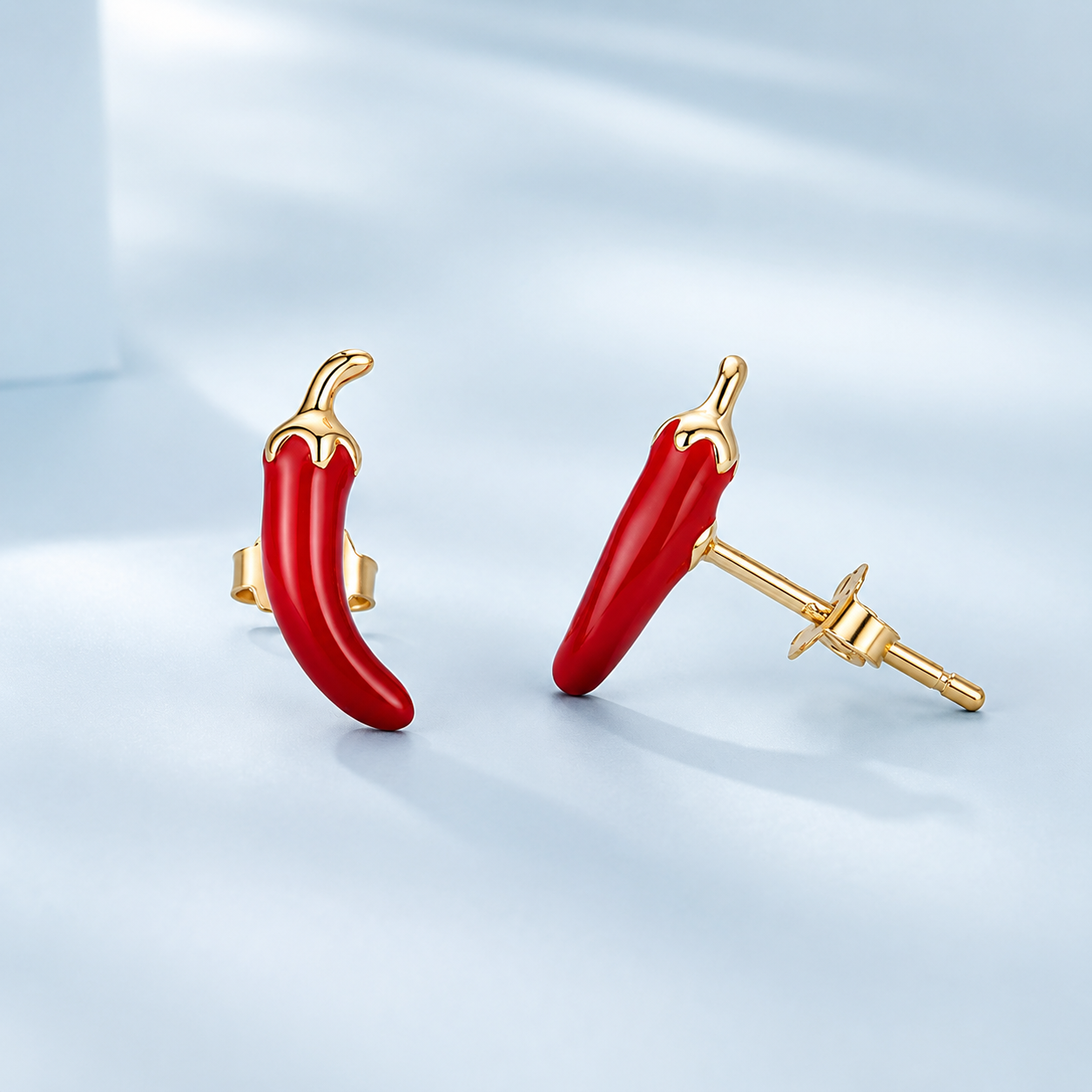 Red chili pepper-shaped earrings with gold posts on a light blue background