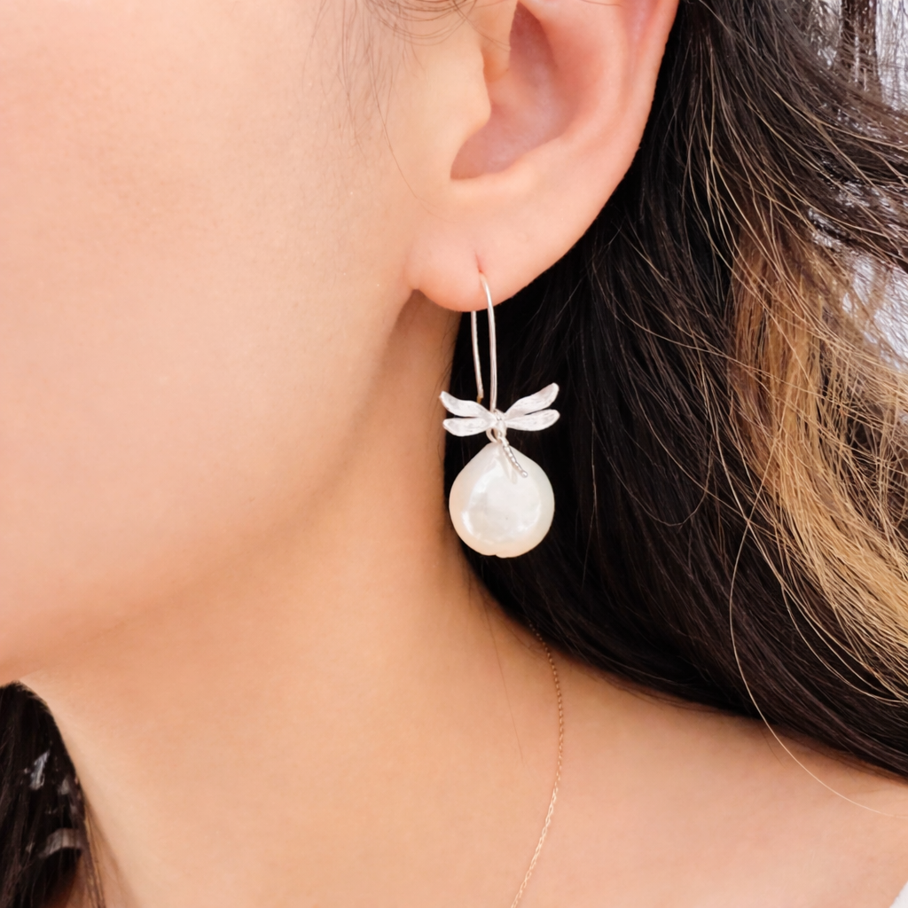 Pearl earring with dragonfly design worn by a person