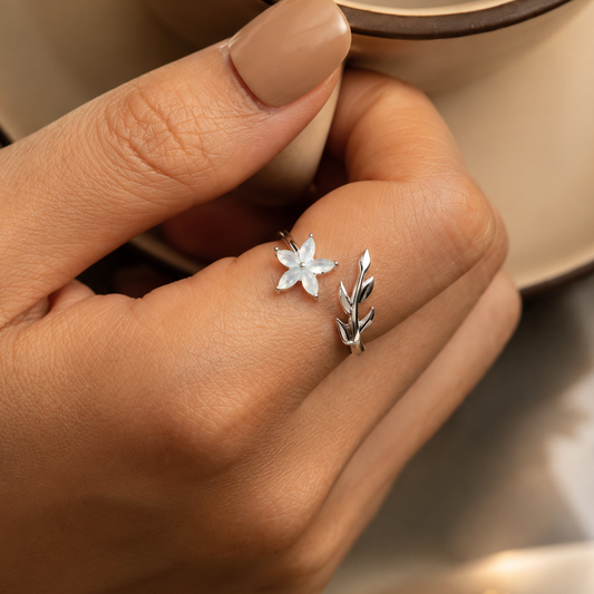 Silver floral and leaf-shaped earrings on a hand against a neutral background